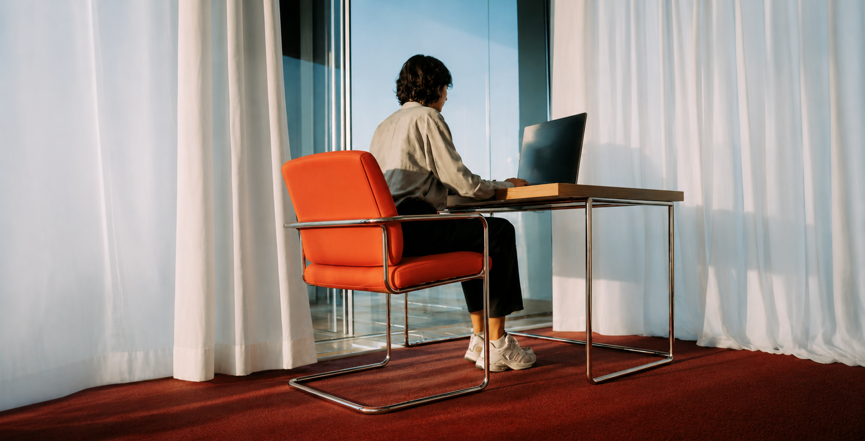 Someone working alone at a laptop by a large window